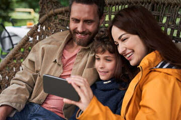 Happy parents and their son using cellphone outdoors