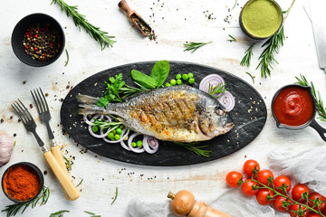 Baked Dorado fish with vegetables on a black stone plate. Top view. Free space for your text.