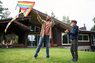 Father and son flying colorful kite on lawn outside the house