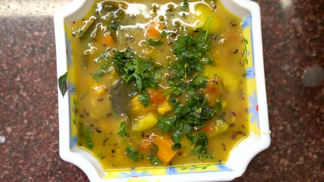Cooked Sambar Dish Garnishing With Freshly Chopped Coriander In A Serving Square Plate. - Close Up - Top Down
