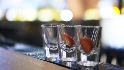 Three shot glasses on bar counter with garnish, on background of bokeh lights. Close up shot of glasses on background of bokeh lights, small shot glasses on table in bar
