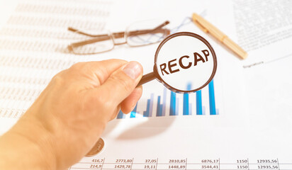 Recap word inscription through magnifying glass on financial documents charts, recap in finance