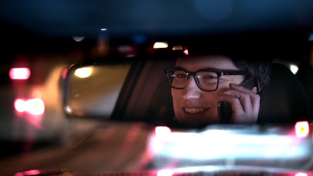 Driver Talking On The Phone, Reflected In A Rear View Mirror, Night Shot. Driver In A Mirror In Car, Night Call On The Road Shot Driving All Night From Backseat