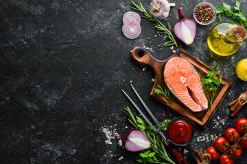 Salmon steak and ingredients on black stone background. Top view. Free space for your text.