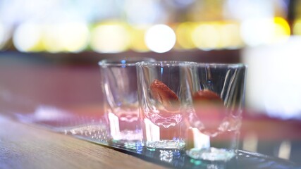 Glasses on bar counter with garnish, on background of bokeh yellow lights. Close up shot of glasses, small shot glasses on table in bar