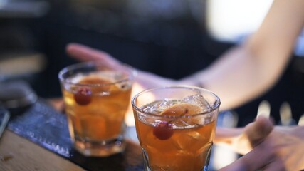 Two glasses with whiskey and ice on bar counter. Close up shot of hand taking glasses of alcohol in bar, blurred background. Two cocktails with ice ready to be served