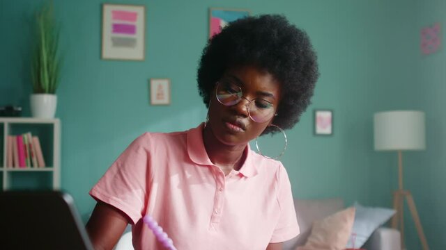 Young black woman is focused on study, sitting at desk at home and makes notes, revising academic material, working hard to pass exam, Foreground, Slow motion.
