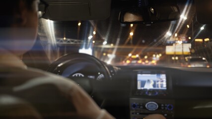 View from back seat of car at night, male driver in eyeglasses back. Night city shot, bokeh lights...