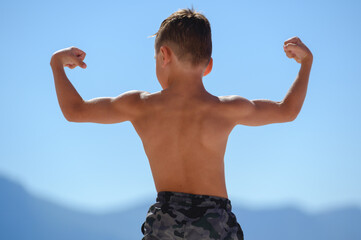 one healthy strong little boy showing back muscles on blue sky and mountain outdoor summer...