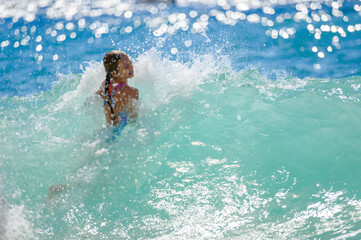 active little thin kid girl in swimsuit jumping on high storm waves in summer blue sea during vacation travel activity