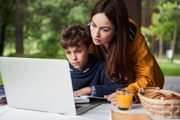Loving mother helping son to do homework outdoors