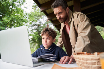 Father and son using laptop while studying outdoors