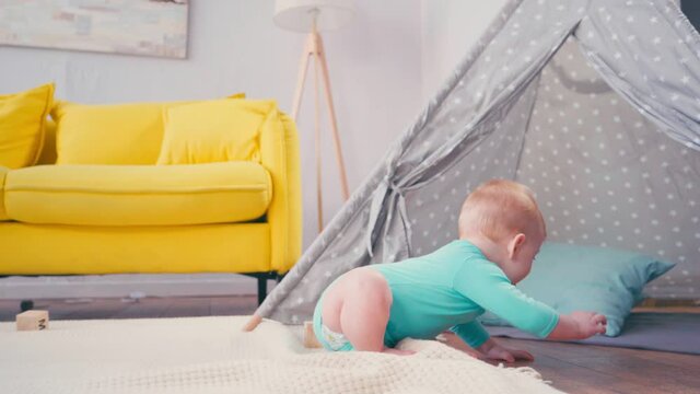 infant boy crawling on blanket near tipi and sofa in living room 