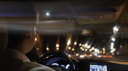 View from back seat of car at night, male driver in eyeglasses back. Night city shot, bokeh lights on the road, taxi driver. Lens flare 