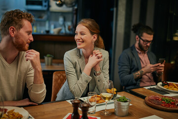 Young couple in love sitting in restaurant with friends and chatting. Night out concept.