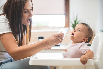 Mother feed her little daughter with a spoon