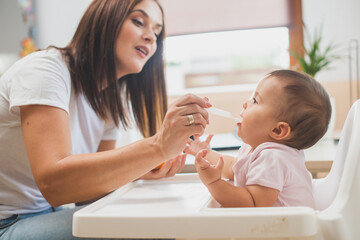 Mother feed her little daughter with a spoon