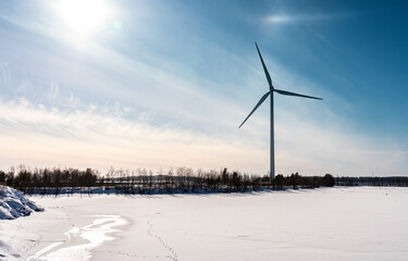 Standalone stopped windmill, no wind. Frozen coast of Baltic Sea. Big Sun spot at sky with white...