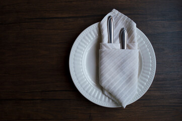 Clean cutlery in a cloth napkin lies on a plate against the background of a dark wooden table....