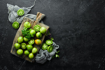 Fresh green tomatoes on black stone background. Green vegetables. Top view. Free space for your text.