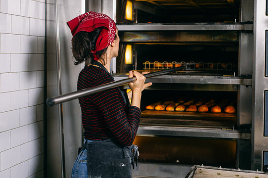Female baker taking bread out oven