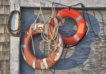 Pair of worn and battered orange rescue lifebuoys hung on side of weathered fishing shack in Spruce...