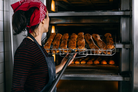 Female baker taking bread out oven