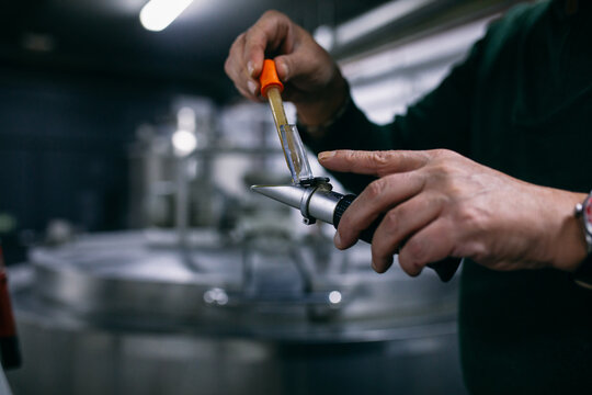 Crop brewer putting beer sample in refractometer