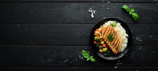 Baked chicken fillet with rice and vegetables on a black plate. Top view. Free copy space.