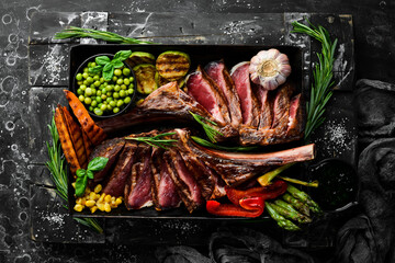 Steak on the bone. Two juicy baked veal steaks with vegetables and spices. On a black background. Top view. Free copy space.