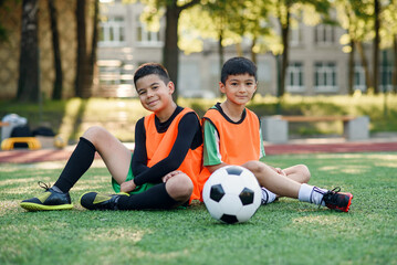 Good-looking joyful teen football players resting on the artificial grass covering of soccer field...