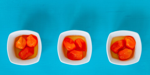 Fermented habanero chili peppers in little bowls. Orange hot chillies against blue background, top...