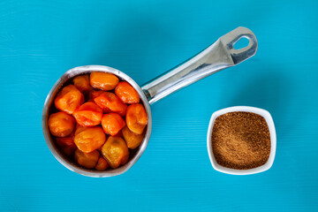 Fermented habanero chili peppers in pot and brown sugar in bowl. Ingredients to prepare hot chili sauce against blue background, top view.