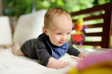 Cute three months old baby boy playing with his toys outdoor. Baby during tummy time. Cute little child learning to crawl.