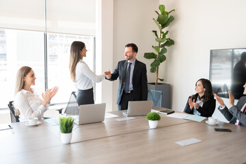 Boss handshaking with successful female employee in meeting