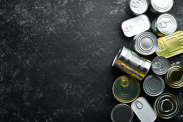 Obraz na płótnie Canvas Set of tin cans with food on black stone background. Food stocks. Top view. Free space for your text.