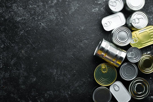 Set of tin cans with food on black stone background. Food stocks. Top view. Free space for your text.