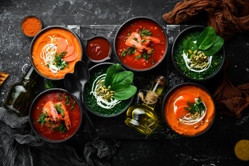 Set of colored soups. Spinach soup, tomato cream soup and carrot puree soup. Healthy food. On a black stone background.