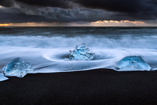 Morceaux de gla&ccedil;ons sur la plage de sable noir de Jokulsarlon avec un ciel orageux