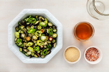 Bowl with cut spicy peppers (various cultivars) and other ingredients to make sliced pickled chillies, top view.
