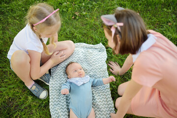 Two big sisters admiring their adorable infant brother. Two young girls holding their new baby boy sibling. Kids with large age gap. Big age difference between siblings.