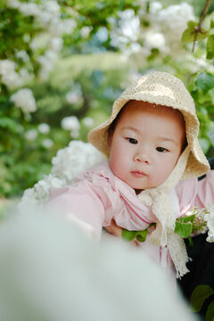 Little girl wearing straw hat on wooden hydrangea background in spring sunshine
