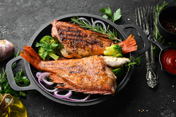 Baked red fish perch with vegetables on a black stone plate. Top view. Free space for your text.