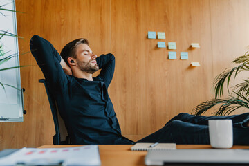 Peaceful young male worker listening music in earphones at office while taking break