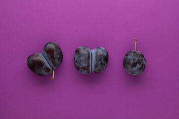 Ugly double plums or prunes on a purple background. Unusual deformed fruits can be used for food. Сoncept - reduce plant or food waste