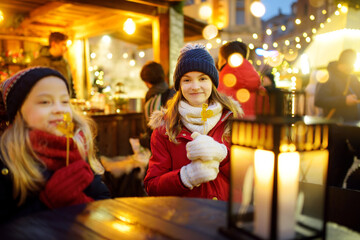Two adorable sisters having rooster-shaped lollipops on traditional Christmas fair in Riga, Latvia. Children enjoying sweets, candies and gingerbread on Xmas market.
