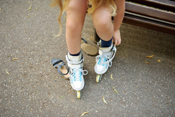 Young girl putting on her inline roller skates on beautiful summer day in a park. Child enjoying...