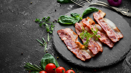Fried bacon slices with basil on a black stone plate. Top view. Free copy space.