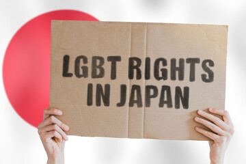 The phrase " LGBT rights in Japan " on a banner in men's hand with blurred Japanese flag on the background. Equality. Human rights. Homosexuality. Love. Pride. Transexual