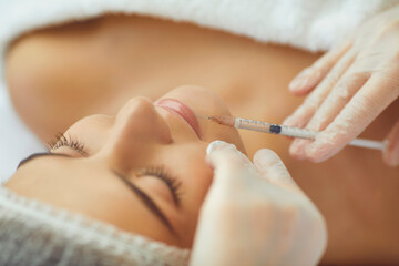 Cosmetologist making botox filler injection in female lips with syringe in beauty salon - obrazy, fototapety, plakaty